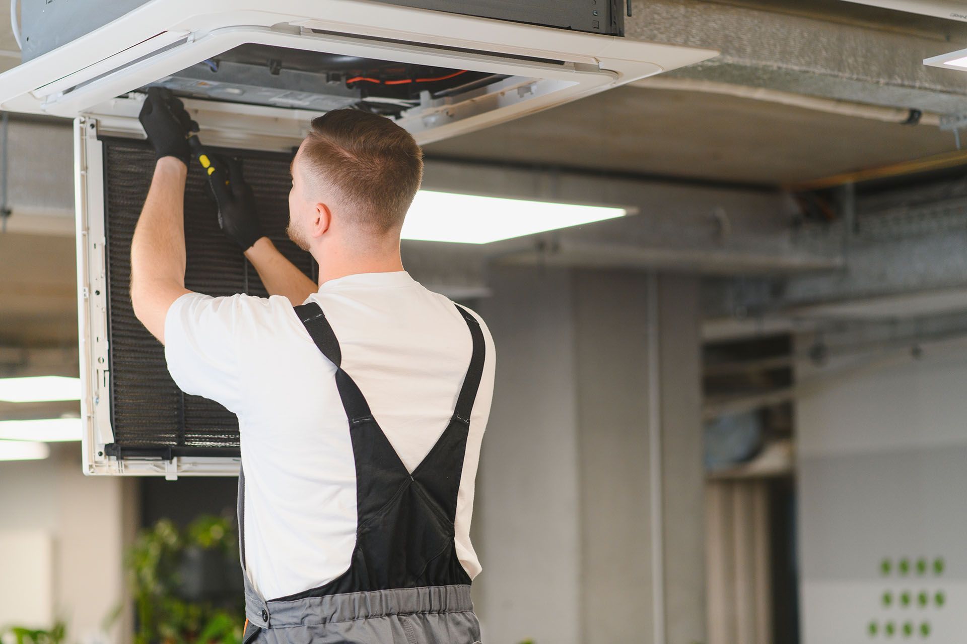 HVAC technician servicing a ceiling-mounted an unit inside a commercial building.