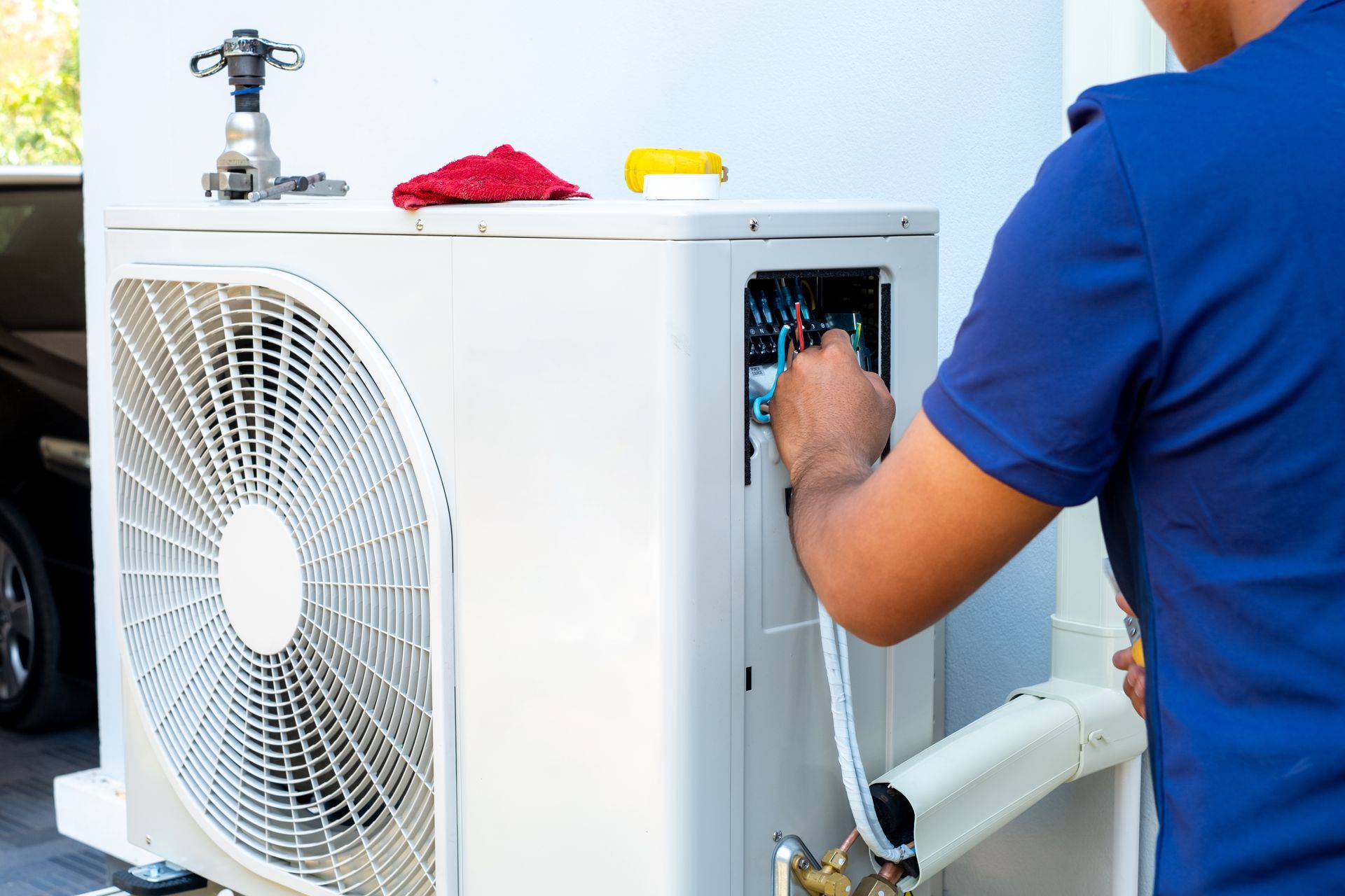 Technician inspecting electrical connections inside an outdoor AC unit.