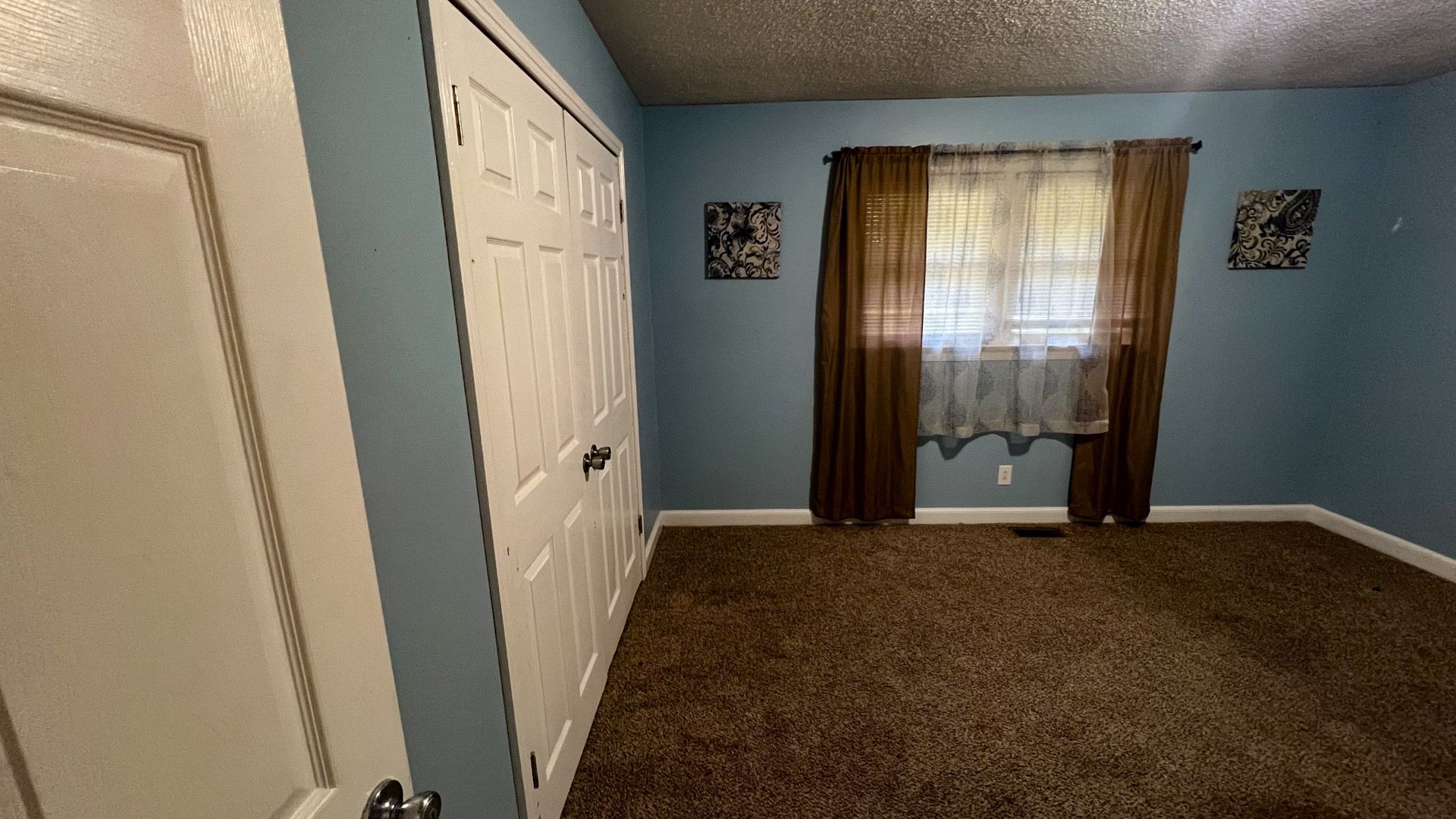 An empty bedroom with blue walls and brown curtains.