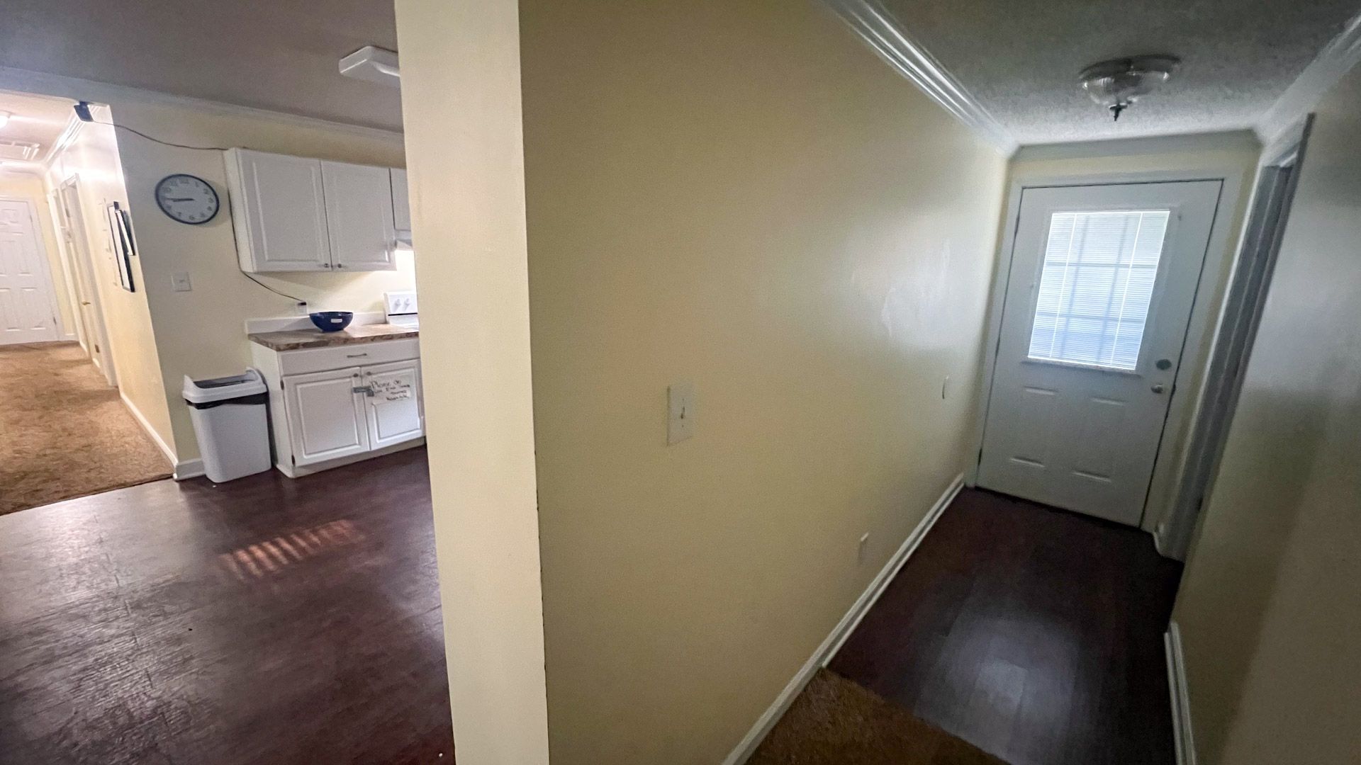 A hallway leading to a kitchen and a door in a house.