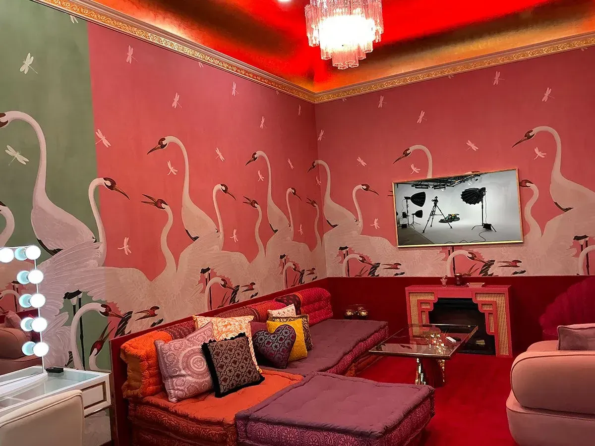 Pink living room with flamingo wall mural, red sofas, and a chandelier.