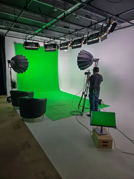 Film studio with green screen, lights, and a crew member adjusting a large softbox setup