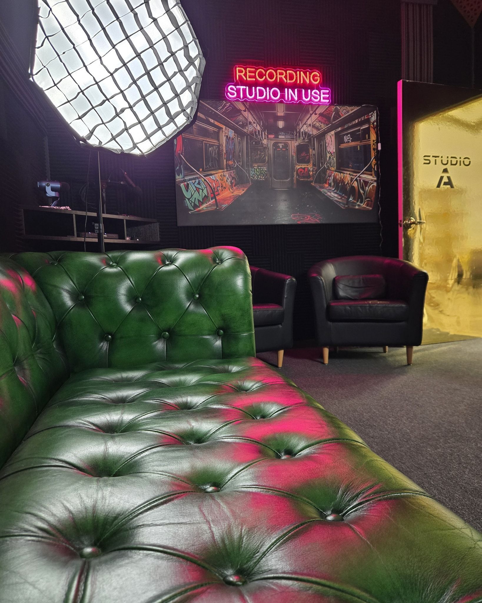 Red tufted chaise lounge in a dim lounge with black chairs and neon pink sign