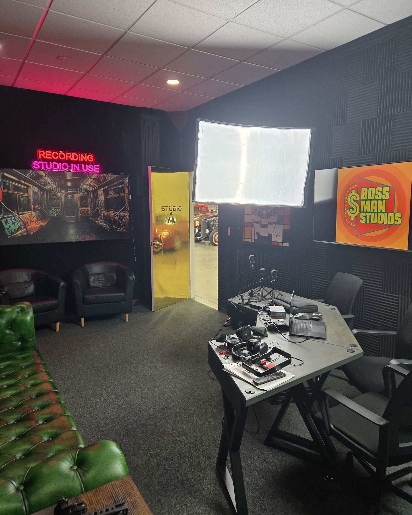 Gaming lounge with neon signs, black chairs, green bench, and a white table in a dark room.