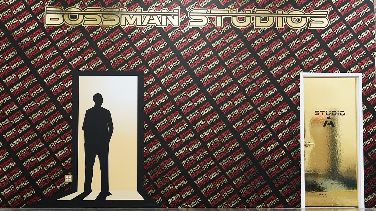 A person stands in a doorway beside a bright yellow wall with a dark red patterned backdrop and sign above.