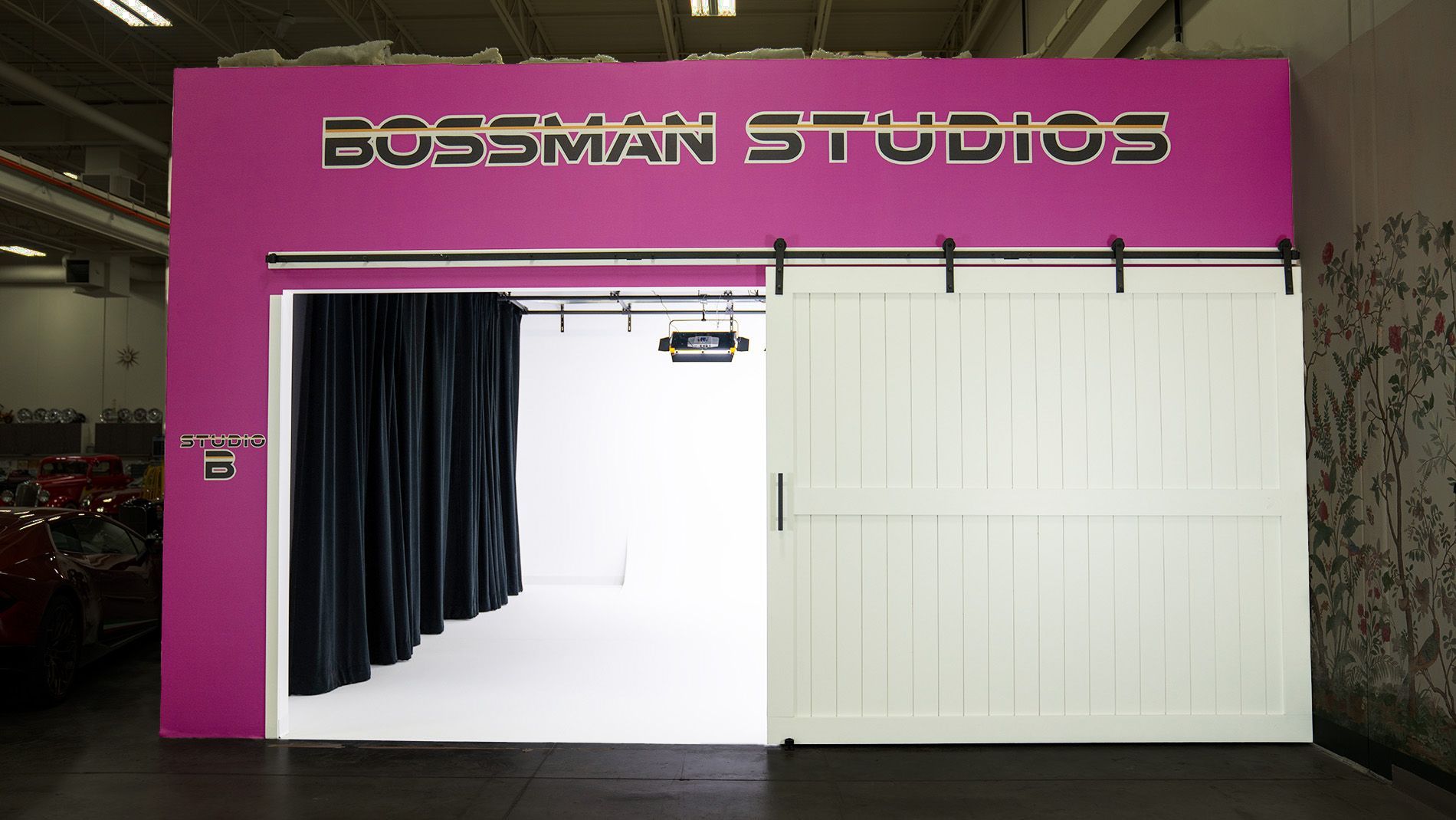 Bright pink Bossman Studios storefront with a large white garage door and open black-curtained entrance