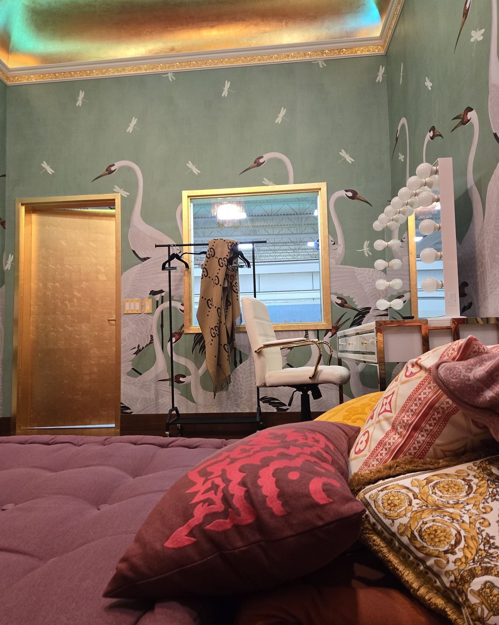 Cozy room with green walls, gold door and mirror, and a mauve couch with patterned pillows.