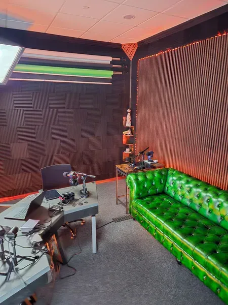Small recording studio with green tufted couch, microphones, and acoustic wall panels.