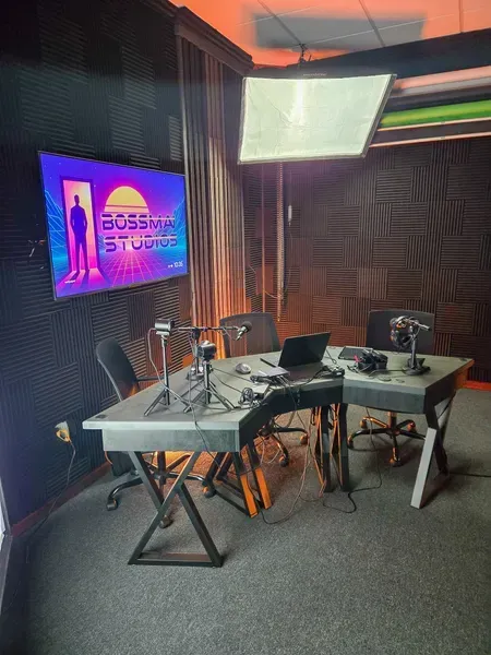 Podcast studio with two microphones, table, laptop, and wall-mounted TV in a soundproof room