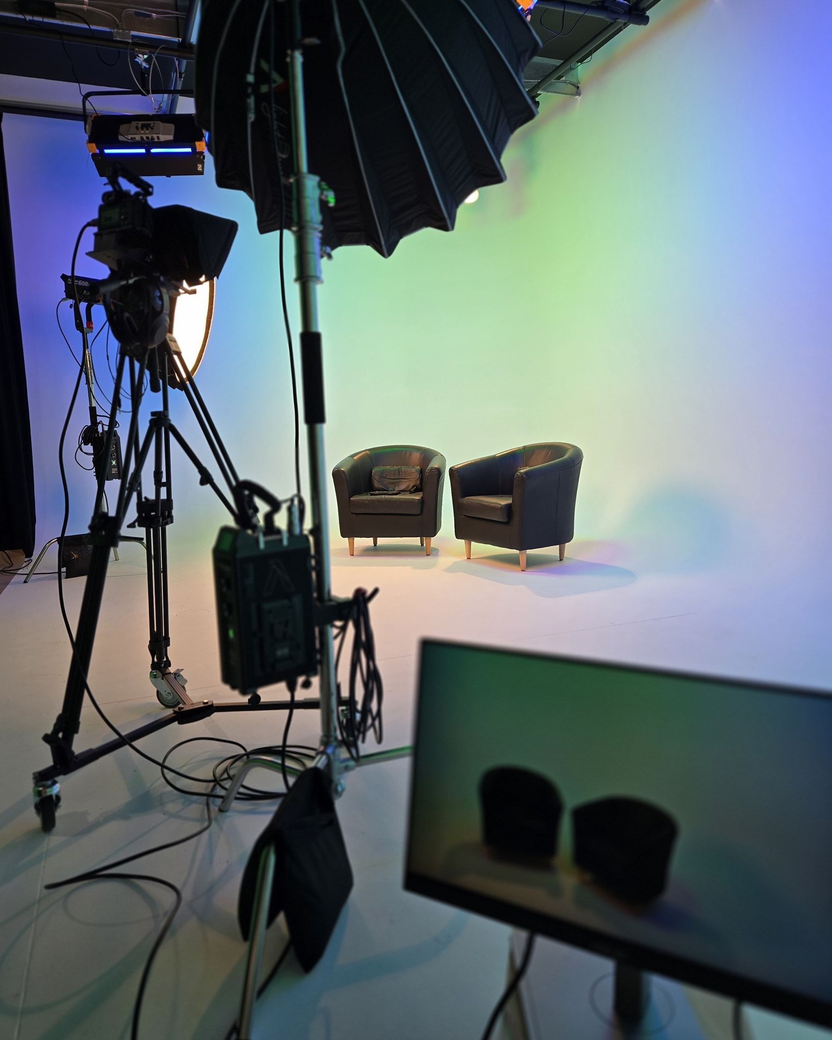 Studio lighting setup with two chairs against a white backdrop and a monitor in the foreground.