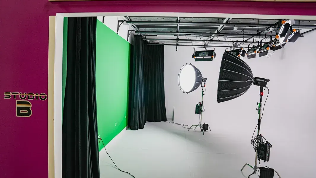Green-screen studio with lighting, backdrop, and camera equipment in a white cyclorama room