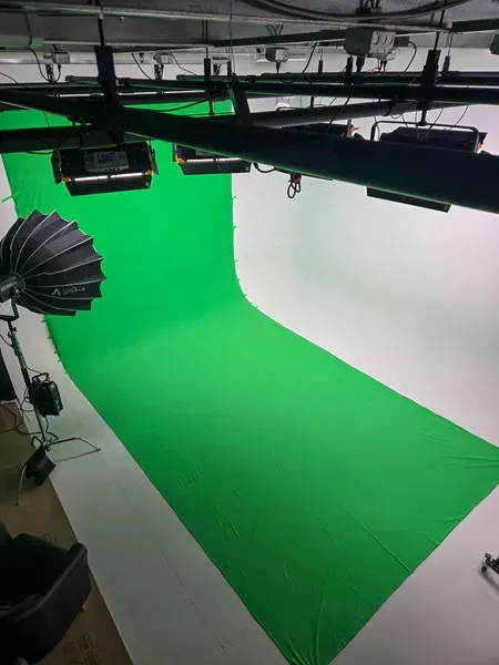 Green screen studio backdrop with overhead lighting and equipment visible