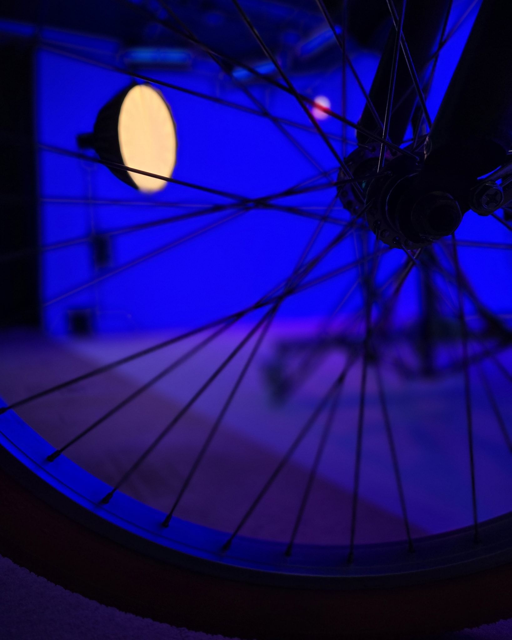 Blue-lit bicycle wheel with spokes and a bright yellow reflector at night