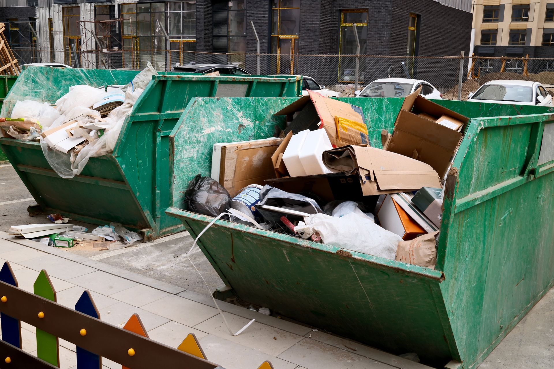 Overflowing green dumpsters piled with cardboard and trash on a city sidewalk