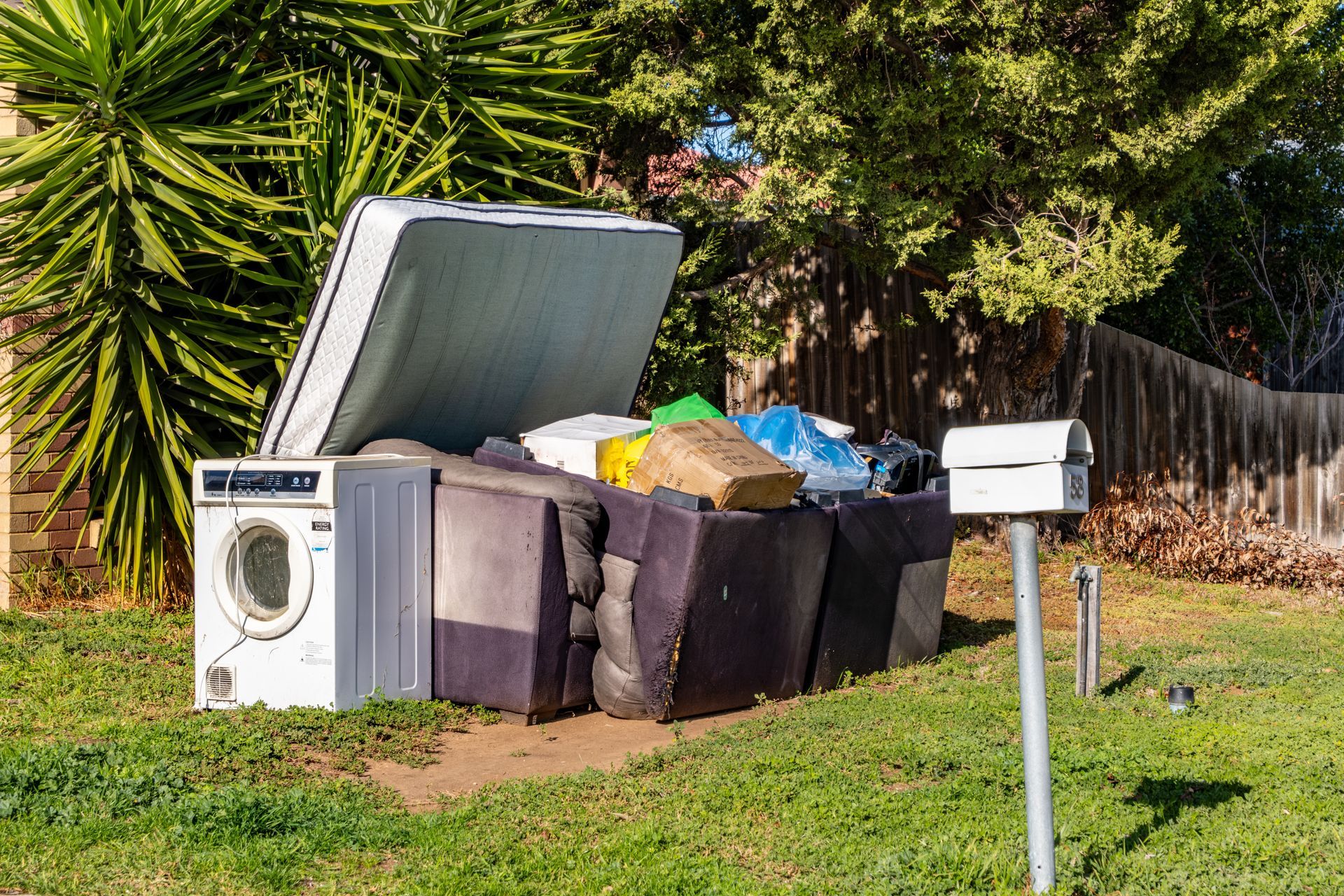 Overflowing curbside trash bins with a tipped-open lid beside a mailbox on a grassy roadside Overflowing curbside trash bins with a tipped-open lid beside a mailbox on a grassy roadside