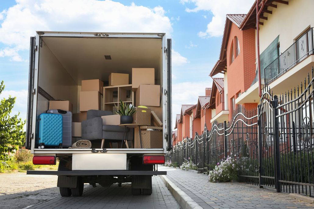 Moving truck loaded with boxes and furniture parked on a residential street beside houses Moving truck loaded with boxes and furniture parked on a residential street beside houses