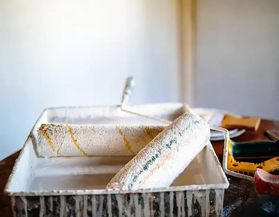Paint roller tray with paint roller and brush on a table, in a softly lit room
