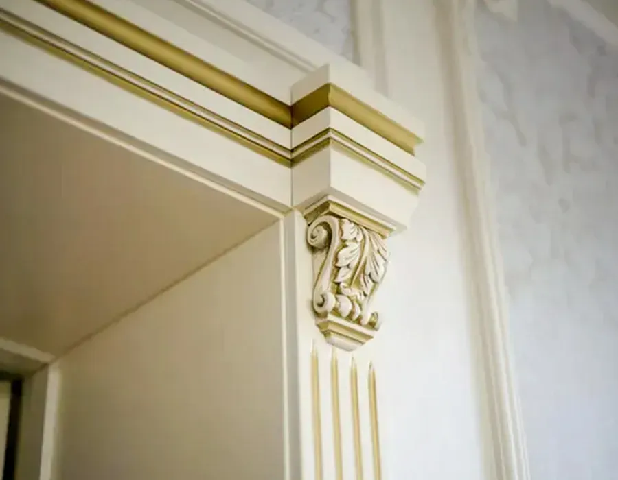 Close-up of an ornate cream-colored doorway trim with gold accents in a bright interior room