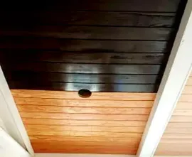 Wood-paneled ceiling with dark and light sections, white beams, and a round recessed light fixture