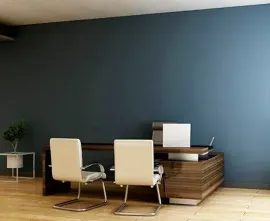 Modern office with two beige chairs, wooden desk, laptop, and a dark blue wall