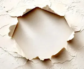 A hole torn through a textured beige wall with rough, cracked edges