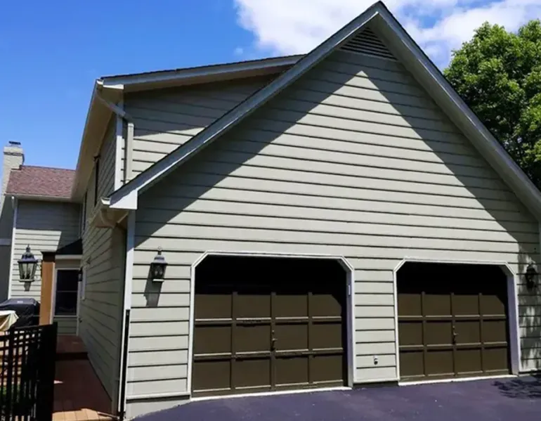 Two-car garage with beige siding and dark brown doors on a sunny residential house