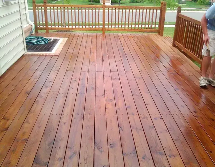 Wooden deck with a railing and a small mat by the house, viewed from above.