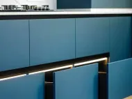 Blue kitchen cabinets with a black countertop and under-cabinet lighting.