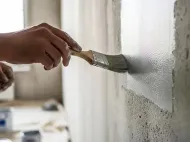 Hand painting a gray wall with a paintbrush in a room under renovation