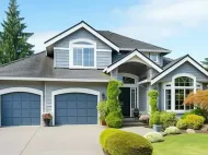 Two-story gray suburban house with blue garage doors, manicured lawn, and landscaped front yard