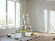 Bright room with open window, stepladder, paint supplies, and drop cloths during home renovation