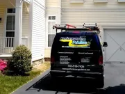 Black service van with roof ladder parked in a driveway beside a beige house.