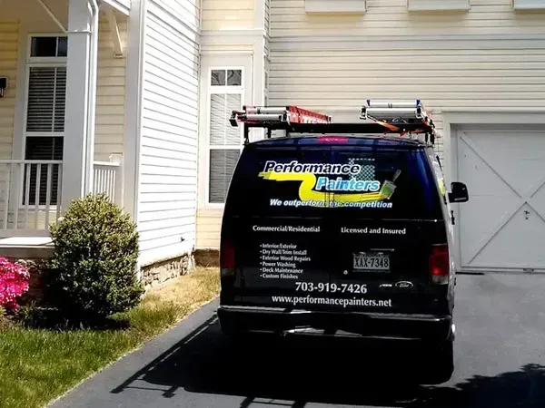Black service van with roof ladder parked in a driveway beside a beige house.