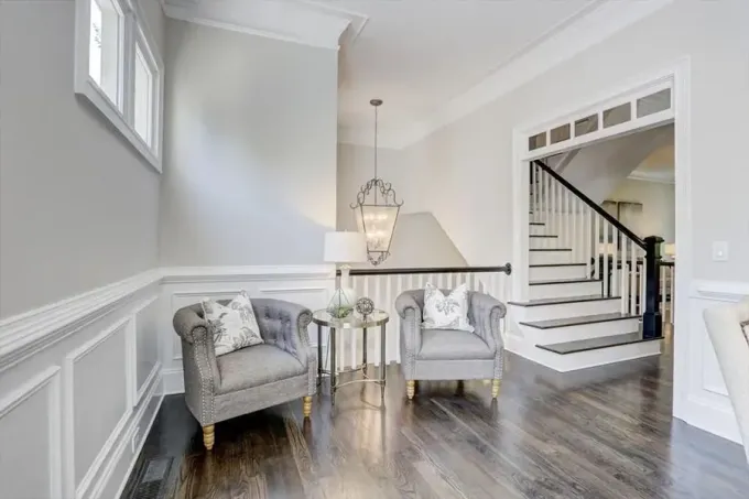 Bright entryway with two gray chairs, a small table, staircase, and dark wood floor