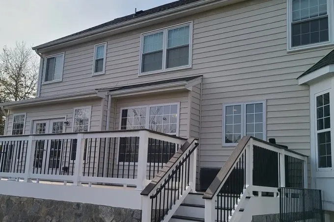Two-story beige house with white porch railing, front steps, and snow on the deck and ground