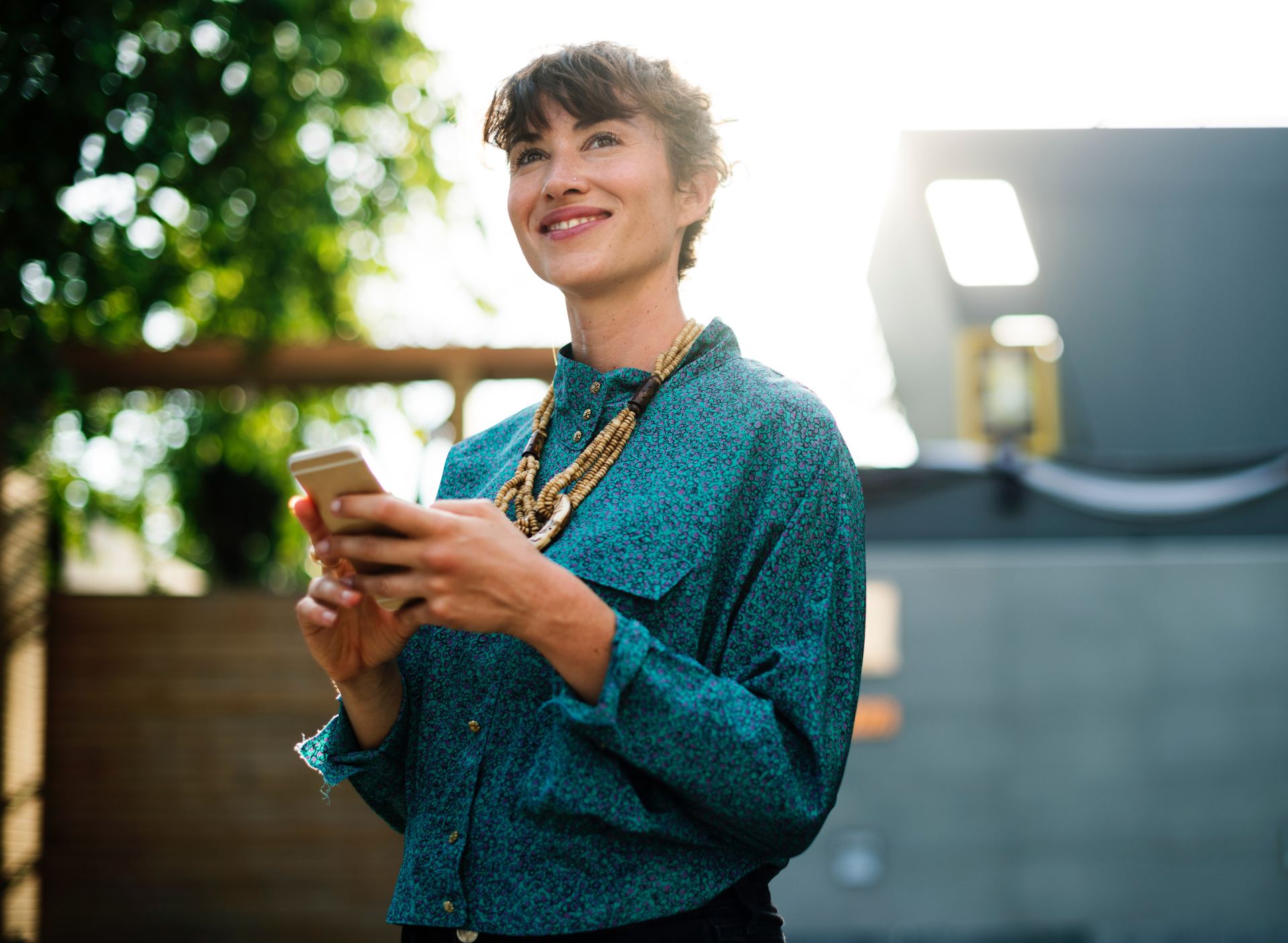 A woman in a blue shirt is holding a cell phone and smiling.