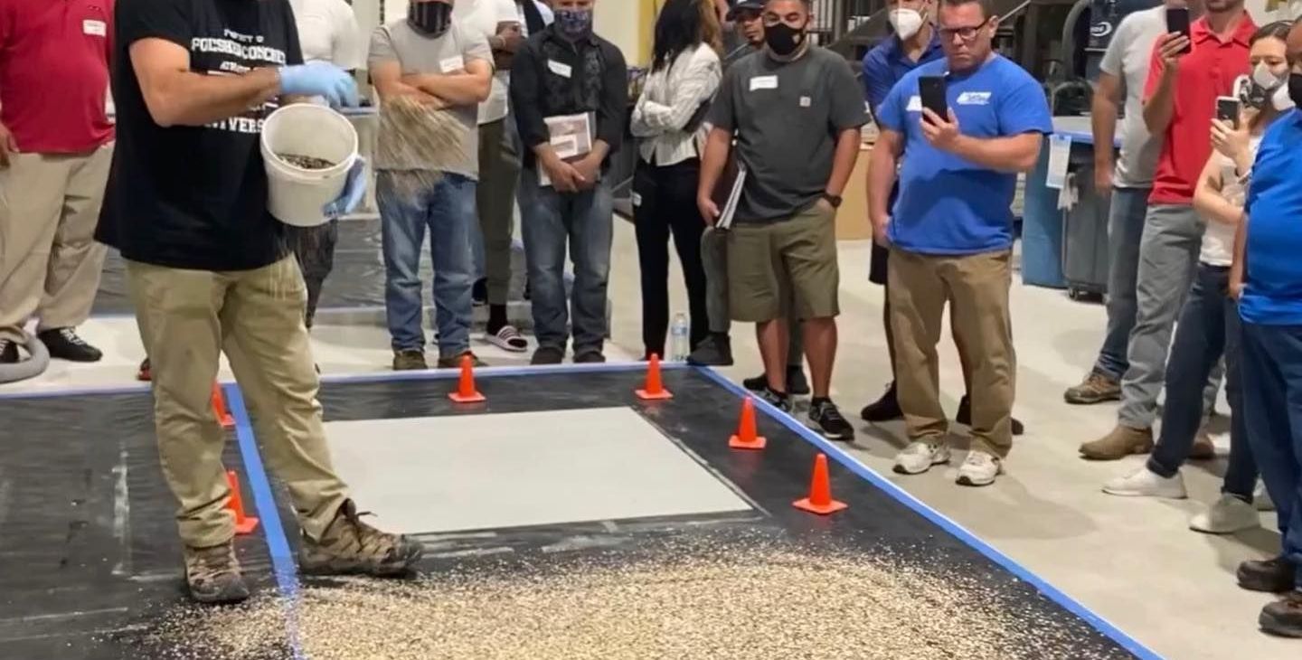 People standing around a demo area with a large white board and orange cones on a concrete floor.