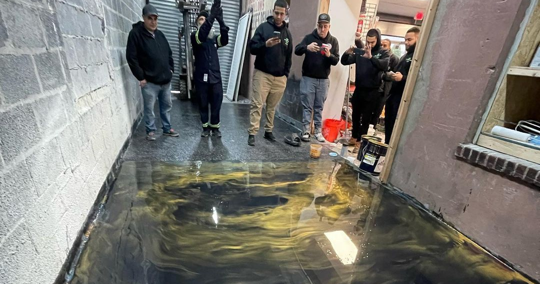 People standing beside a flooded alley with a dark, reflective puddle across the ground