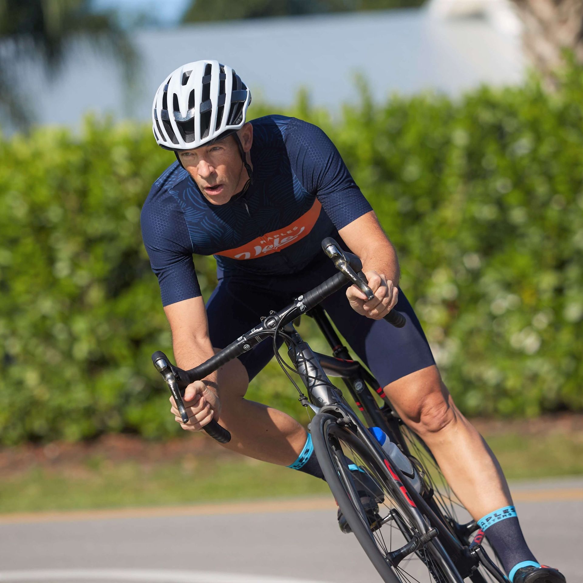 Cyclist Michael Ceely in a blue jersey and white helmet leans into a turn on a road.