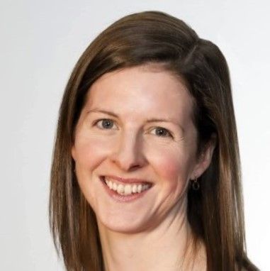 Studio headshot of a smiling woman with brown hair on a light background