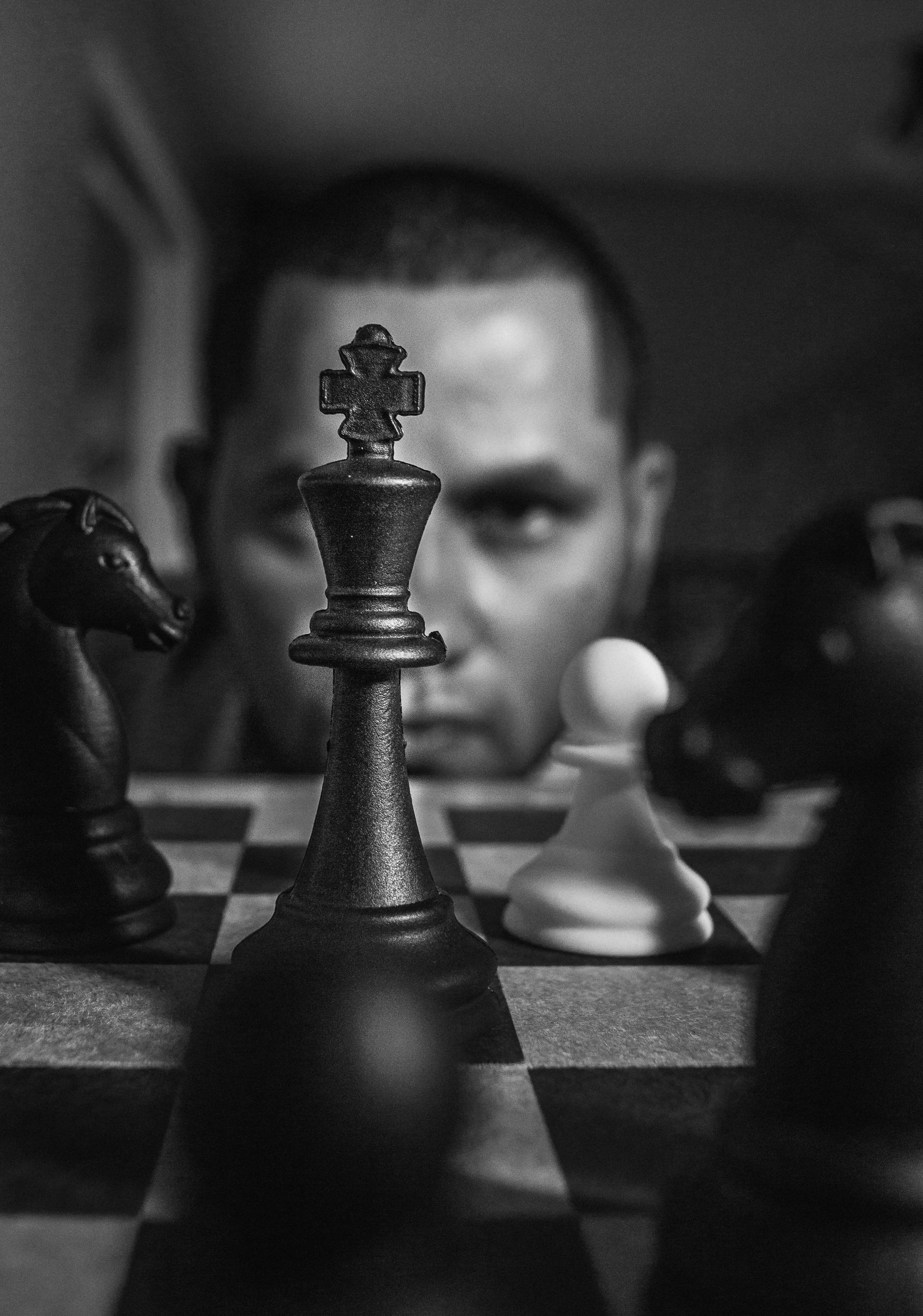 Chess pieces in focus with a man staring intently in the background.