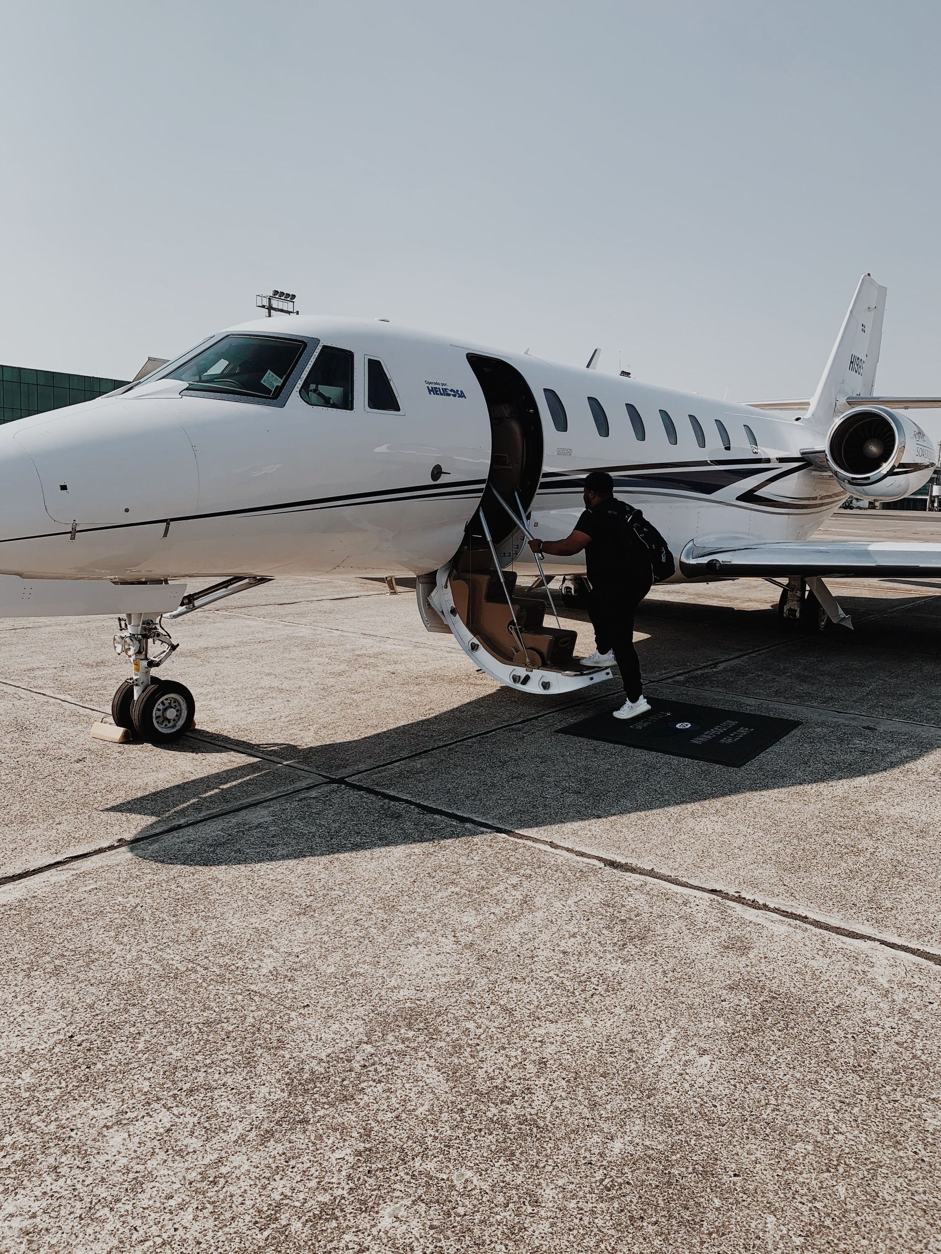 Private jet on tarmac with open door and stairway, a person boarding in bright sunlight