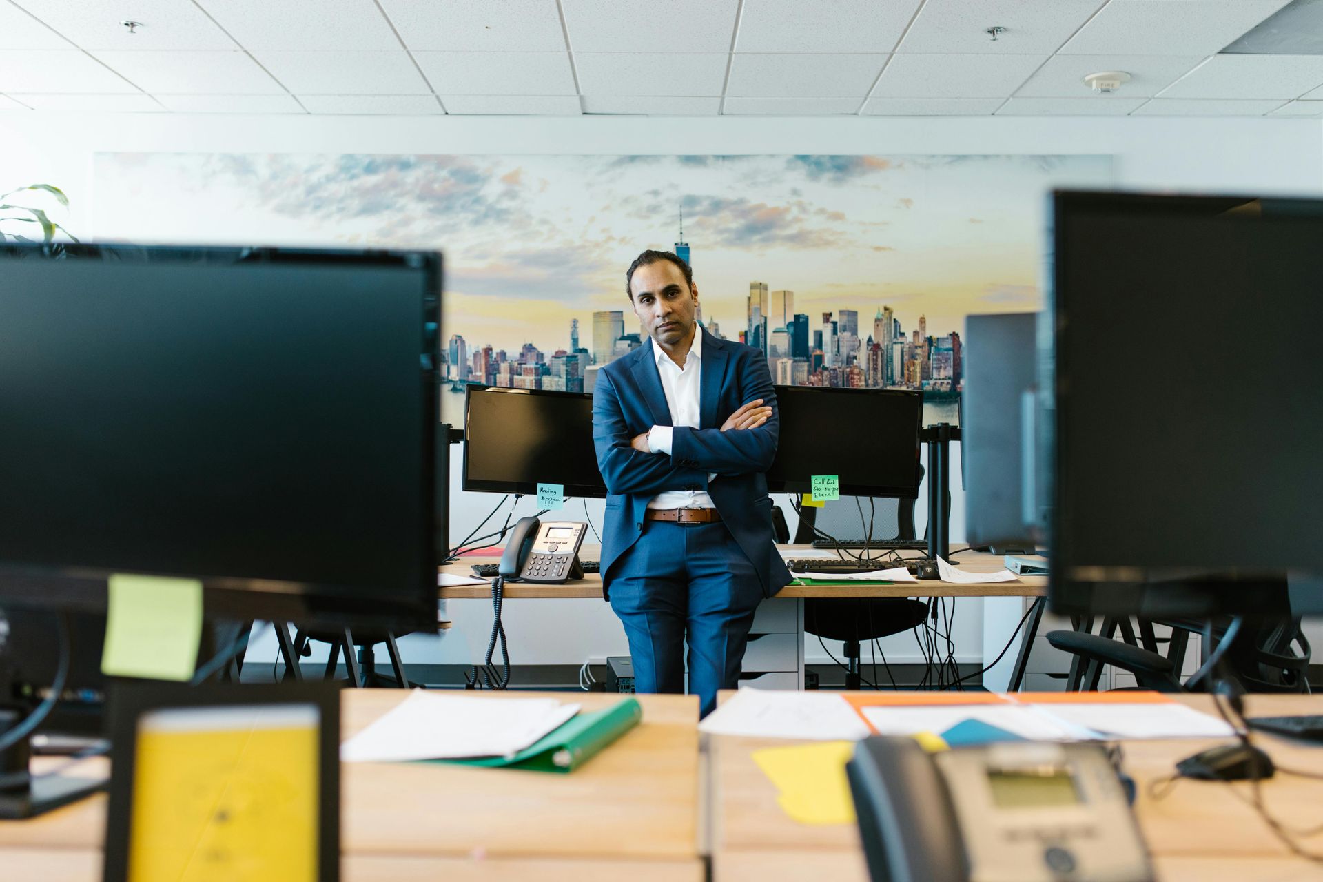 Businessperson standing in a modern office between computer monitors, arms crossed