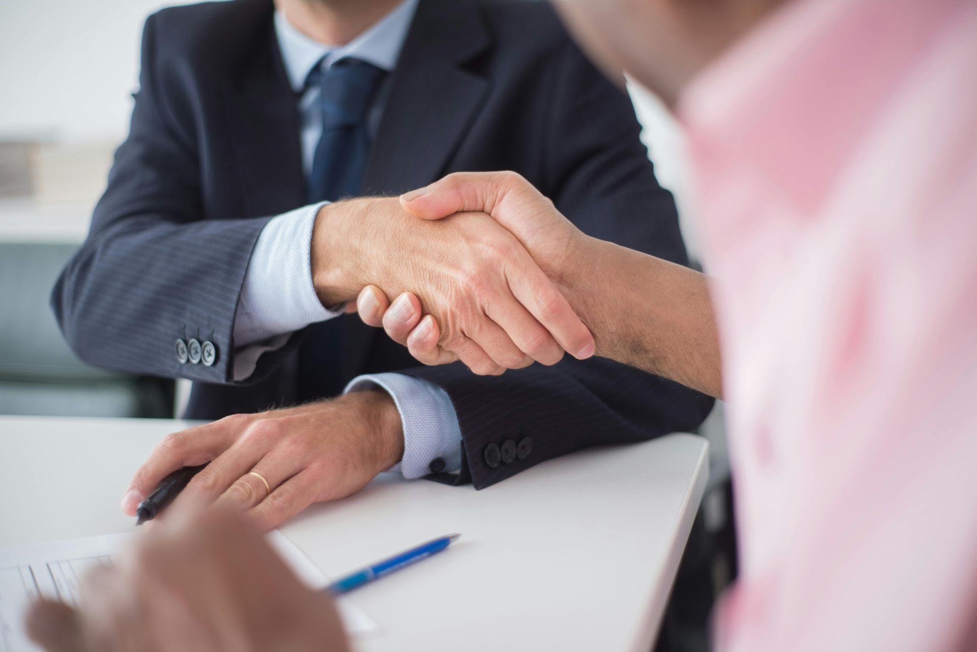Two men are shaking hands while sitting at a table.