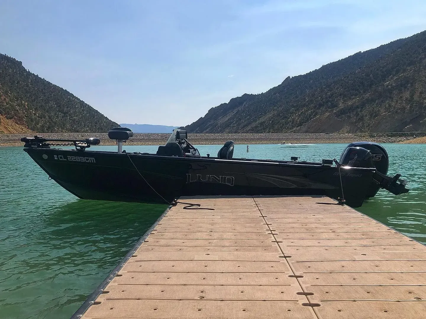 Dark boat docked on a pier; mountains in the background, blue sky and water.