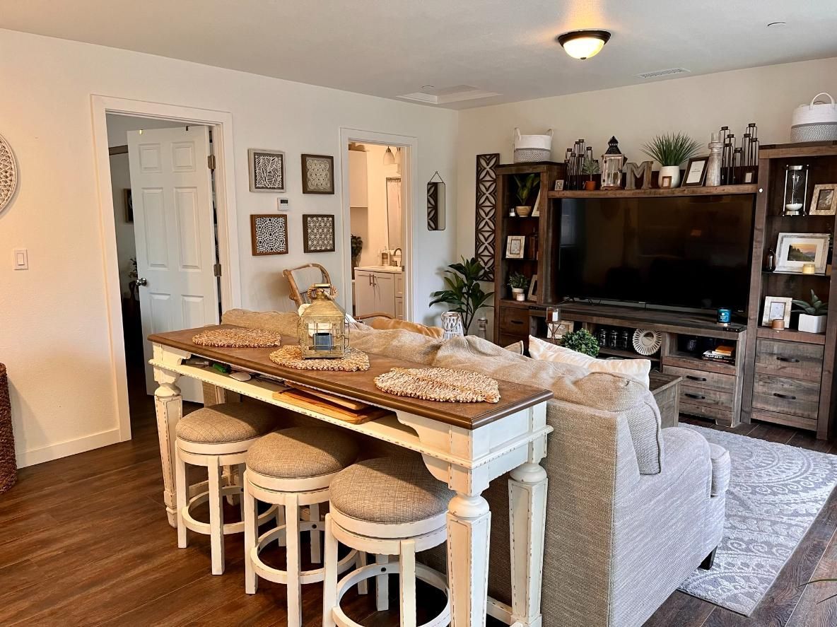 Open living room and dining area with a round table, stools, couch, TV, and shelves in warm neutral tones