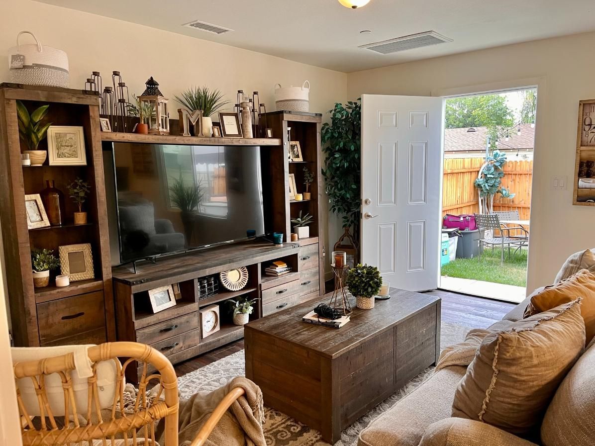 Cozy living room with TV, wooden furniture, plants, and open door to a sunny patio