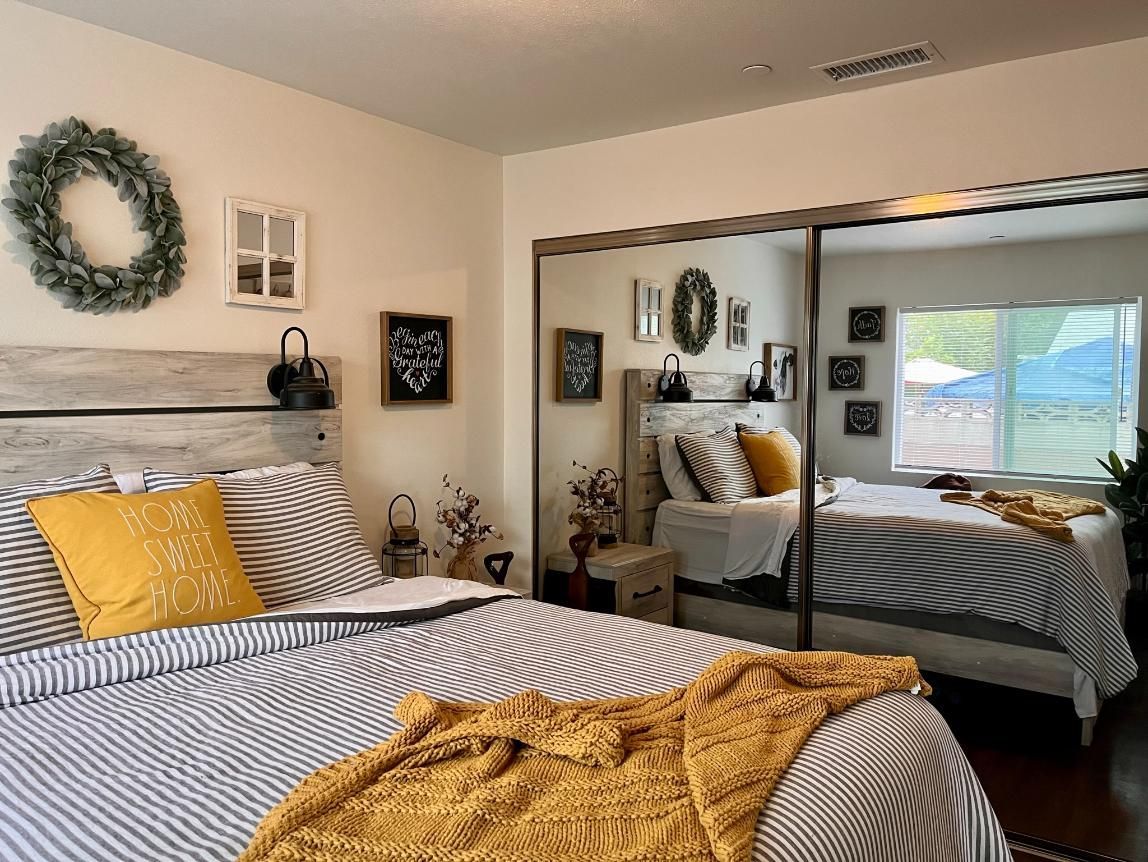 Cozy bedroom with striped bedding, yellow pillow and blanket, wreath decor, and mirrored closet doors reflecting the room.