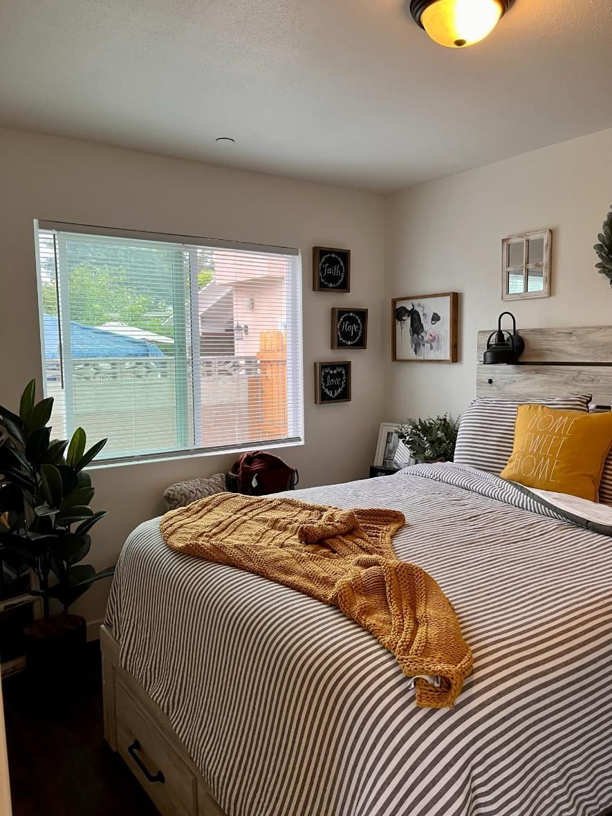 Cozy bedroom with made bed, yellow blanket, window light, wall art, and potted plant