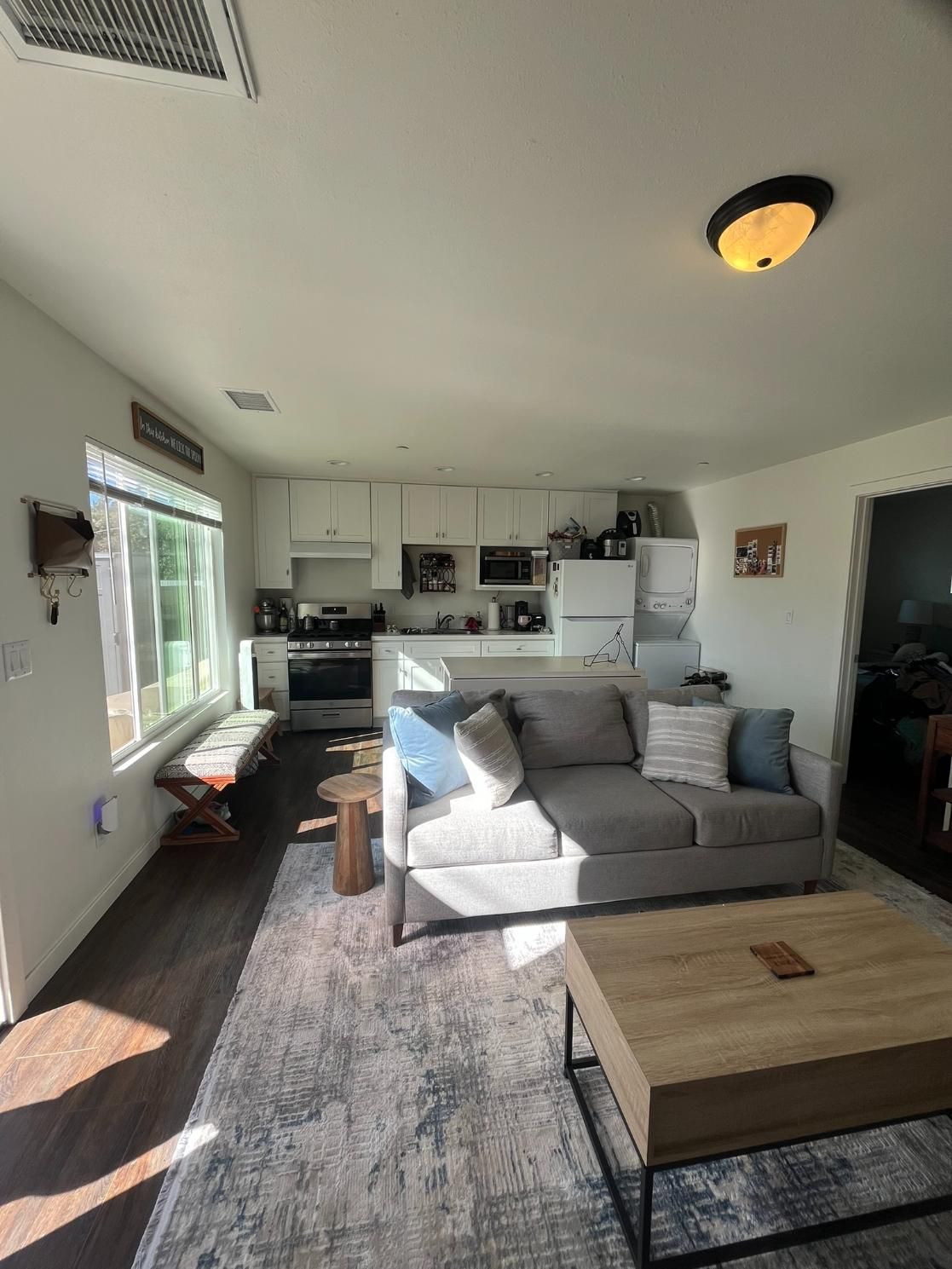 Bright living room with gray sofa, coffee table, rug, and open kitchen in the background.